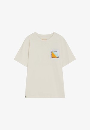Camiseta de manga corta color crema con un pequeño parche gráfico colorido en el pecho izquierdo que incluye texto e íconos de botón de reproducción.