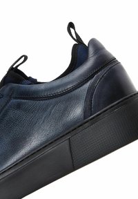 Baskets en cuir bleu foncé avec semelle en caoutchouc noire texturée et languettes en tissu au talon et à la languette.