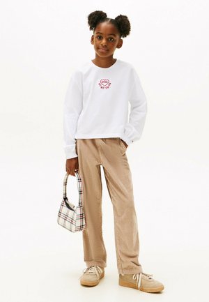 Weißes Langarmshirt mit roter Herzstickerei, beigem Cordhosen und einer karierten Handtasche. Beige Sneakers mit weißen Schnürsenkeln.