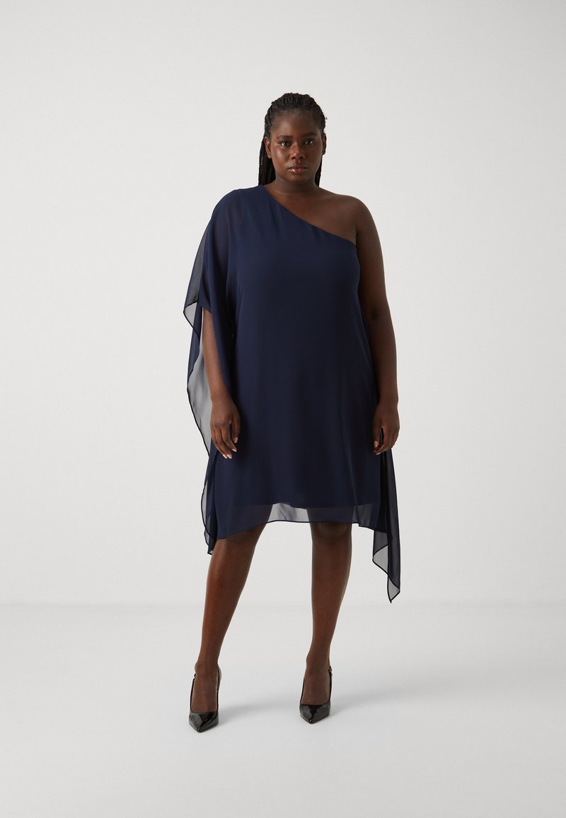 Robe bleu marine à une épaule avec un superposé fluide et transparent. Présente une coupe ample et une longueur au genou. Portée avec des talons noirs pointus.
