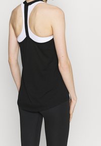 Débardeur de sport noir avec des accents blancs, présentant un design dos nageur et une texture lisse. Porté avec un legging noir.