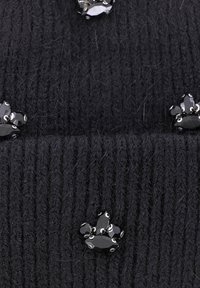 Beanie nero a maglia con texture a coste, decorato con diverse applicazioni di gioielli neri disposte in un design a impronta di zampa.