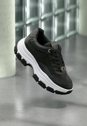 Sneaker de sport noir avec tissu texturé et accents en cuir. Présente une semelle intermédiaire blanche, une semelle extérieure noire robuste et un détail de logo doré.