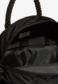 Černý batoh s pletenými tkaninovými uchy, zapínáním na zip a hladou saténovou vnitřní podšívkou. Viditelná štítek uvnitř. Minimalistický design.