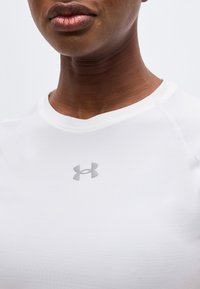 Κοντινή λήψη ενός ατόμου που φοράει λευκό πουκάμισο Under Armour, με το λογότυπο στο στήθος και μέρος του κάτω μέρους του προσώπου και του λαιμού.