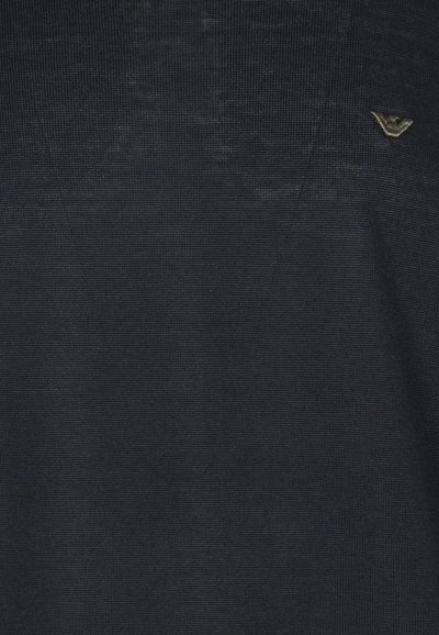 Maglietta a maglia blu navy con tessuto testurizzato, caratterizzata da un piccolo logo metallico in alto a sinistra. Design semplice e senza motivi distintivi.