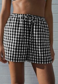 Schwarz-weiße karierte Shorts mit einem elastischen Bund, Kordelzugverschluss und zwei Seitentaschen. Leichtes, strukturiertes Material.