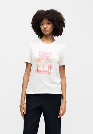 Woman with curly hair wearing a white t-shirt with pink text "Lucky Girls Club" and pastel palm tree graphic, paired with black pants.