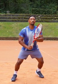 Tennis player with a blue gradient shirt and gray shorts, preparing to hit a ball on a clay court, holding a red and white racquet.