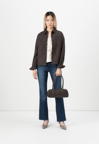 Brown suede button-up jacket, cream top, blue flared jeans, gray heeled shoes, and a dark brown handbag. Simple and structured design.