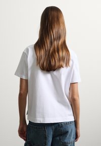 T-shirt bianco in cotone con maniche corte e una vestibilità leggermente oversize, abbinato a pantaloni corti in denim larghi con grandi tasche posteriori.