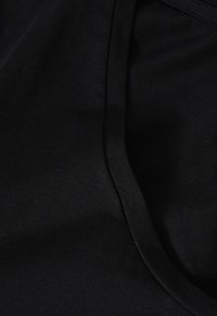 Schwarzer Stoff mit glatter Textur, der eine gebogene Kante und sichtbare Nähte aufweist. Das Material wirkt leicht und flexibel.