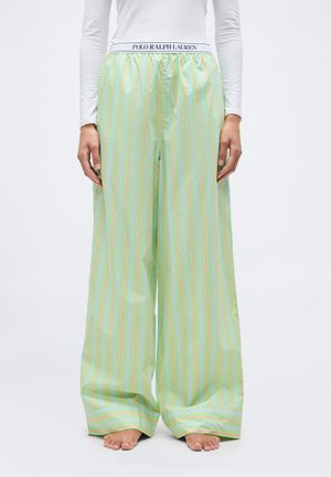 Blootsvoetse persoon die pastelgroene broek met wijde pijpen draagt, met verticale roze en blauwe strepen en een witte tailleband waarop 'Polo Ralph Lauren' staat.