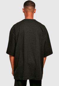 Tricou oversized negru, cu mâneci scurte, guler rotund, din material de bumbac, textură netedă, design simplu, fără modele sau accente vizibile.
