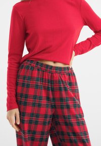 Red long-sleeve top with vertical ribbed texture, paired with red plaid pants featuring green and black check patterns and button detail.