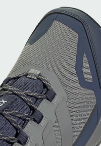 Nahaufnahme eines atmungsaktiven Sneakers in Grau und Marineblau mit gemusterten Schnürsenkeln und verstärkter Zehenkappe, die Textur und Nähdetails hervorhebt.