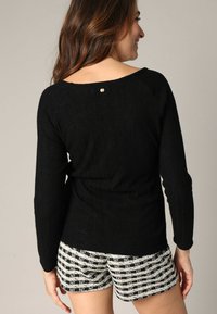 Un pull noir en tricot avec un large décolleté et une texture côtelée, associé à un short à carreaux noir et blanc. Présente un détail en accent doré.