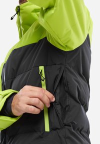 Schwarze und neongrüne Daunenjacke mit Reißverschlusstasche. Das Material ist glatt und weist kontrastierende Farben sowie sichtbare Nähte auf.