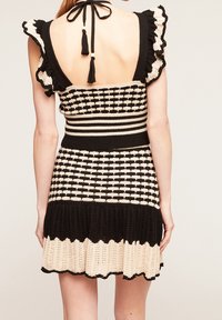 Svart och krämfärgad virkad klänning med rygglös design, volangärmar och mönstrad byst. Har en utsvängd, scallopad nederkant.