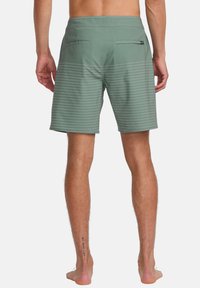 Bañadores de hombre en verde con rayas blancas horizontales. Cuenta con dos bolsillos traseros y una cintura plana. El material parece suave y ligero.