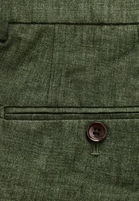 Green linen fabric with a textured appearance, featuring a single brown button and a pocket detail. Structured, with fine stitching accents.
