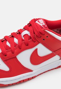 Adidași Nike roșii și albi, cu superior din piele, limbă căptușită, șireturi groase și sigla distinctivă Swoosh. Talpă din cauciuc texturat.