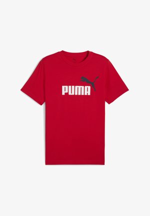 Rdeča bombažna majica s kratkimi rokavi, ki ima velik bel logotip "PUMA" in črn silhueto pum. Ima okroglo ovratnik.