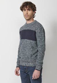 Suéter de punto en azul y gris con un bloque sólido texturizado en color marino a lo largo del pecho. Puños y dobladillo acanalados con un diseño de cuello redondo.