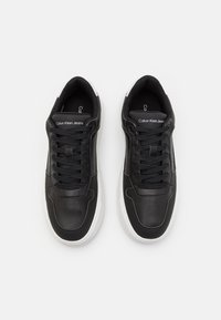 Sneaker in pelle nera con suola in gomma bianca, dotate di lacci neri piatti e branding "Calvin Klein Jeans" sulla linguetta. Texture liscia.