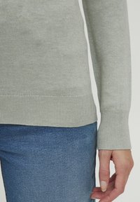 Light gray knitted sweater with ribbed cuffs and hem. Fabric appears soft with a fine texture. Paired with blue denim fabric.