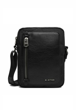 Černá kabelka G-Star přes rameno s texturovanou přední kapsou, vertikálním zipem a nastavitelným popruhem s logem na bílém pozadí.