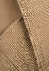 Cotton fabric in a muted beige color, featuring fine diagonal ribbing and visible stitching, highlighting texture and seam detail.