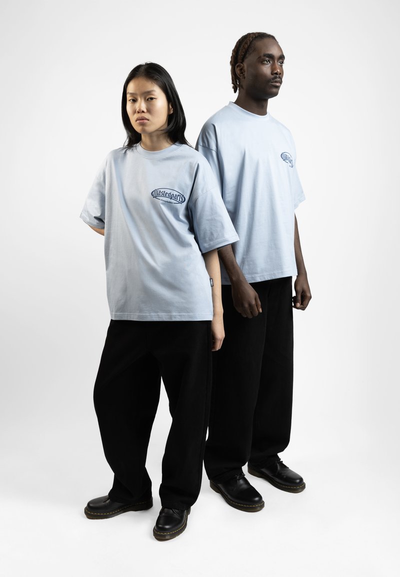 Light blue oversized t-shirts with a logo, paired with black wide-leg pants and black shoes, on a plain white background.