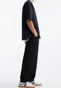 Sort oversized T-shirt med korte ærmer parret med sorte cargo-bukser. Hvide sneakers med grønne og sorte detaljer. Enkel, afslappet design.