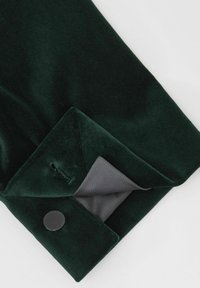 Tume roheline sametkangas volditud mansetiga. Mansetis on must nupp ja sile hall vooder, mis on nähtav manseti sees.