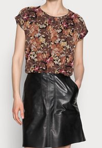 Haut à motif floral dans des tons marron, orange et rose, avec des manches courtes ; associé à une jupe en cuir noire avec poches avant et détails de couture.