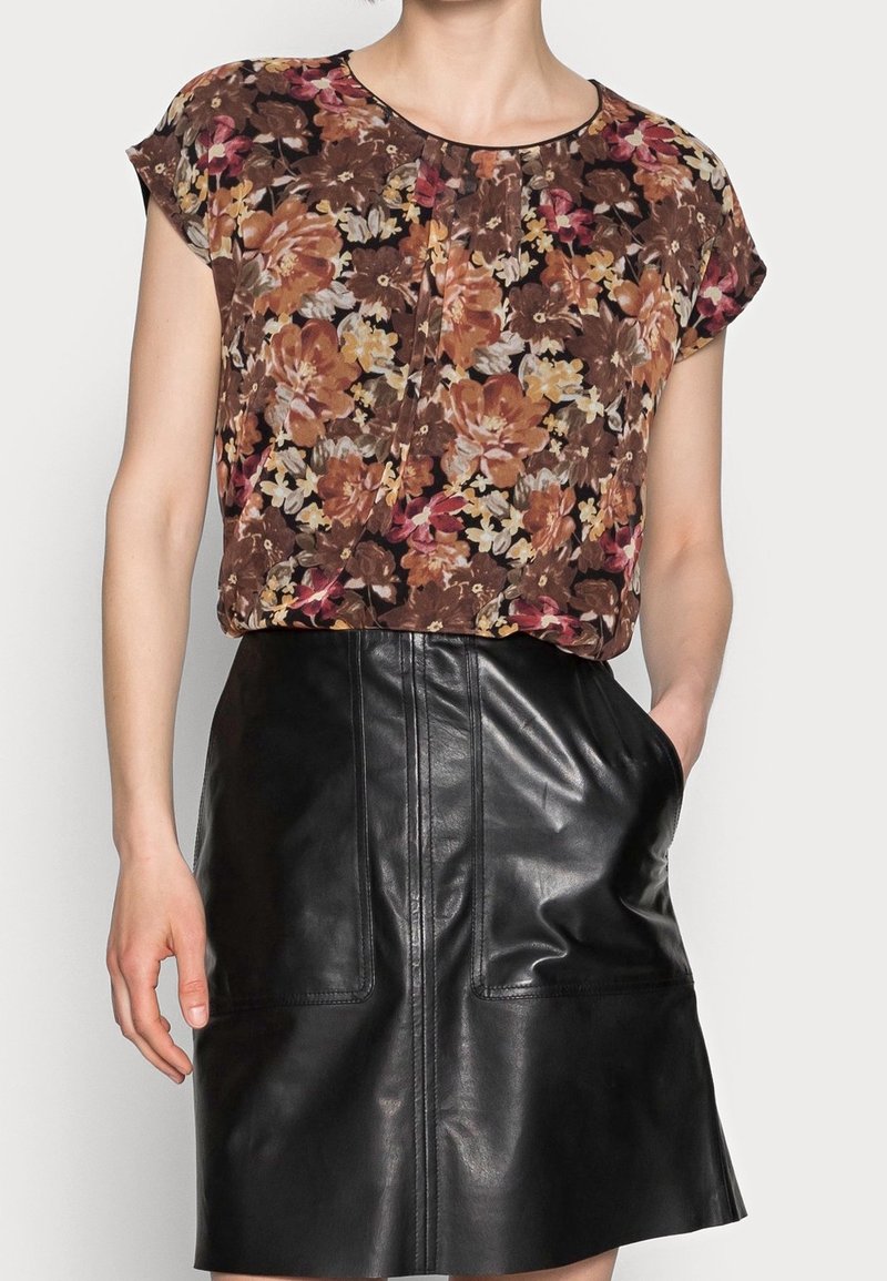 Haut à motif floral dans des tons marron, orange et rose, avec des manches courtes ; associé à une jupe en cuir noire avec poches avant et détails de couture.