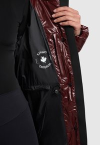 Sötét színű külső ruházat fényes bordó béléssel, logó címkével, patentgombokkal és belső állítható fém kiegészítőkkel.