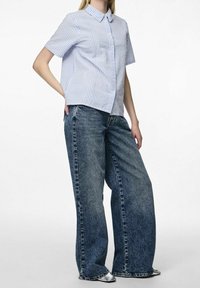 Camicia a maniche corte con colletto in blu chiaro e bianche strisce verticali, abbinata a jeans in denim blue larghi e strappati.