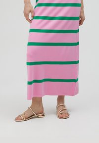 Rosa randig klänning med gröna horisontella ränder, tillverkad av mjukt tyg, i kombination med guldfärgade sandaler med remmar och låg klack.