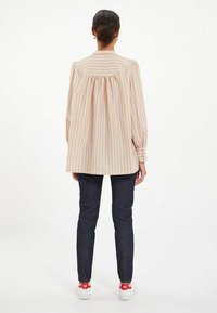 Chemise à rayures beiges claires avec des rayures verticales, coupe décontractée, dos froncé, manches longues et ourlet arrondi. Portée avec un jean foncé.