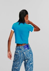 Zkrácené modré tričko s bílými rukávy, spárované s modrými džínami s potiskem a modrou nášivkou na zadní straně.