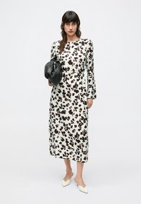 Biele šaty s dlhým rukávom v tvare áčka s hnedo-čiernym zvieracím vzorom, doplnené čiernou kabelkou a párované s topánkami na špičke.