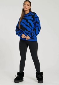 Blå och svart mönstrad tröja med rund halsringning, kombinerad med svarta leggings och fluffiga svarta ankelstövlar. Strukturerad stickad design.