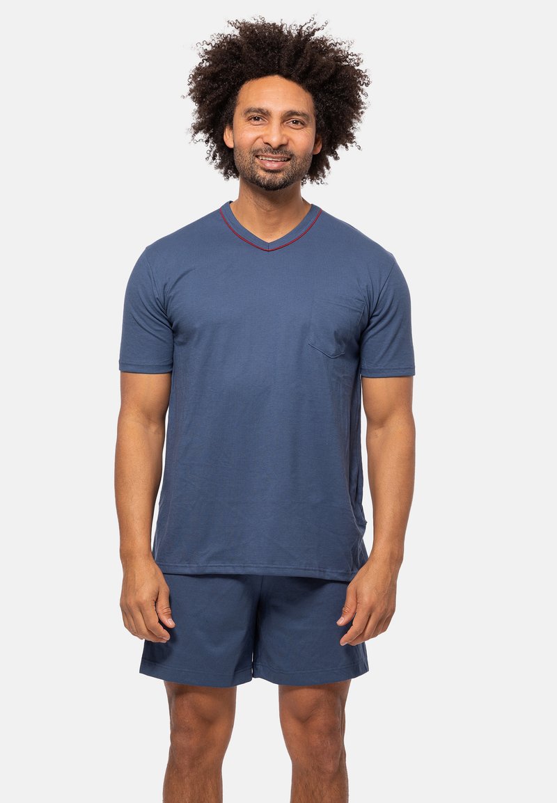 Marineblå T-shirt med kort ærme og V-hals, med sidelomme, og røde kanter, parret med matchende marineblå shorts. Materialet er en bomuldsblanding.