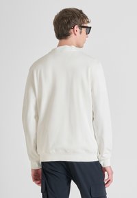 Felpa chiara in crema con collo a giro, texture morbida, maniche lunghe e polsini a coste, abbinata a pantaloni cargo blu navy.