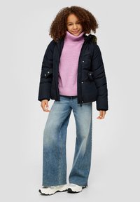 Marineblaue Daunenjacke mit Kapuze, kombiniert mit einem hellrosa Rollkragenpullover und weit geschnittenen blauen Jeans. Die Schuhe sind weiße Sneakers mit Akzenten.