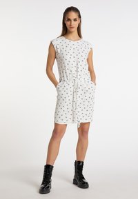 Hvid kort kjole med sort blomsterprint, rund halsudskæring og kortærmer. Har en elastisk talje med bindebånd og sidelommer.