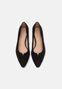 Black suede flats with pointed toes and a rounded cutout. Features a bow accent at the front and a smooth interior lining.