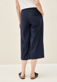 Navy culottes met een relaxte pasvorm, elastische tailleband en zijzakken. Heeft een gladde textuur en een cropped lengte. G gedragen met sandalen met open achterkant.